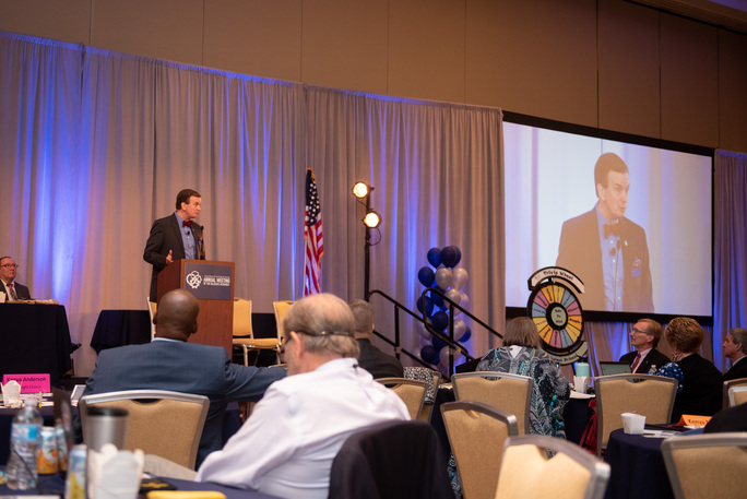 photograph taken at annual meeting of Harold Dean speaking at a podium to delegates.
