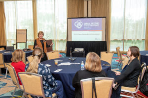 photograph of Mary Jo Monahan speaking to a group seated at a round table.