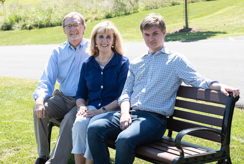 Photo of three people sitting on a bench, outdoors, on a sunny day