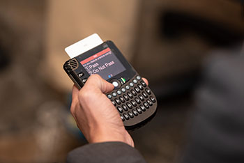 Photo of a person's hand holding an electronic voting keypad. The screen on the keypad reads "1. Pass. 2. Do Not Pass."