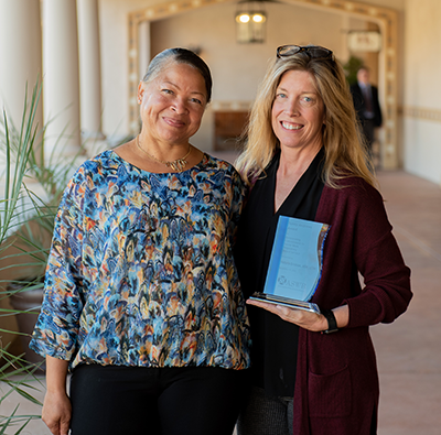 Photo of two women, both smiling. The woman on the right is holding a plaque.