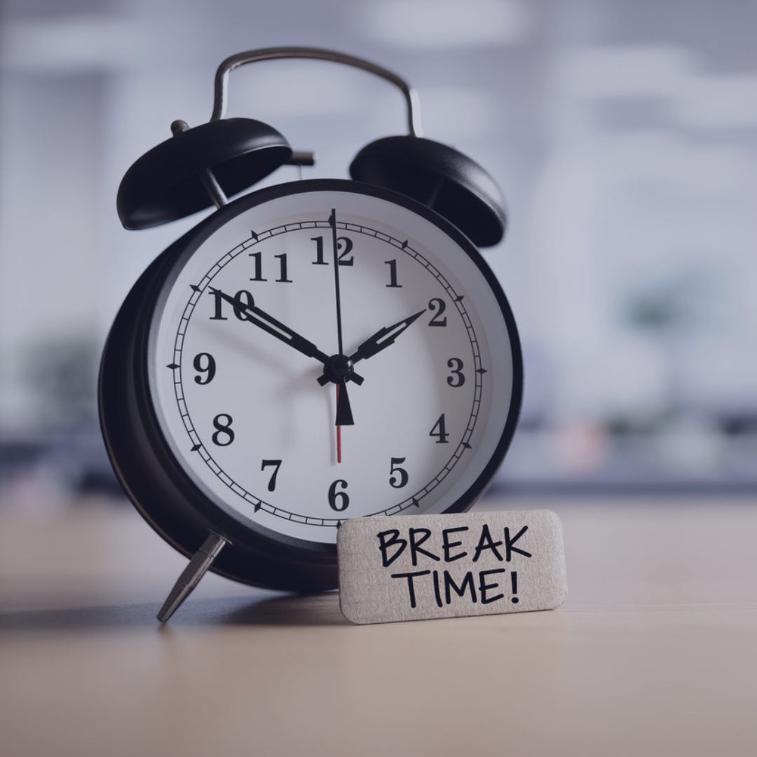 Photograph of an alarm clock sitting off-center on a table. There is a piece of paper with the writing "Break Time!" written on the paper.