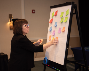Photograph of a woman putting a sticky note on a flipchart with other colorful notes
